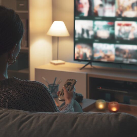 Donna seduta sul divano, con in mano un telecomando, mentre sceglie contenuti dalla sua smart TV.
